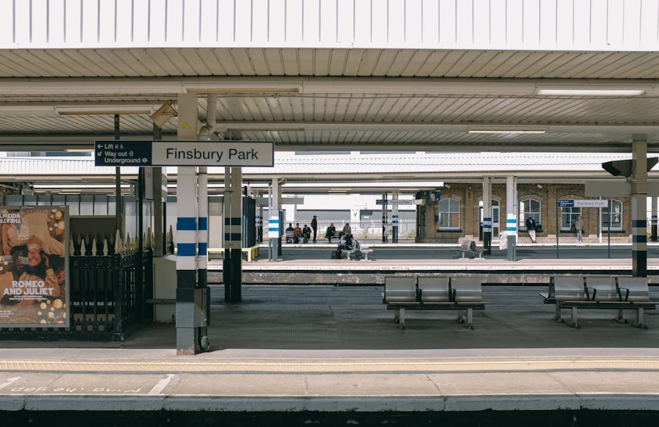 Limited view of Finsbury Park station platform with a white sign displaying 'Finsbury Park', benches, and waiting passengers in the background under a metal canopy, with an adjacent advertisement post