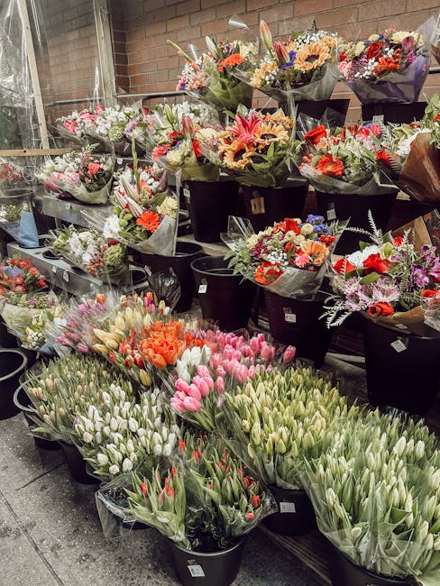 A display of numerous flower bouquets and arrangements at a florist shop, featuring a variety of fresh flowers including pink, orange, red, purple, and white blooms. The bouquets are wrapped in black